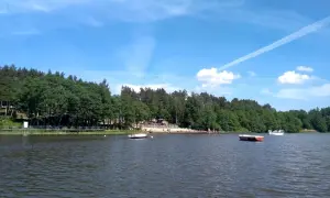 Letnie popołudnie nad jeziorem Osuszyno. Woda spokojna, na brzegu plażowicze, a na jeziorze łodzie. Może nawet jakieś ryby pływają pod powierzchnią.
