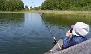 Osoba łowi ryby nad jeziorem, ciesząc się spokojem. Posiada zezwolenie PZW Wrocław.