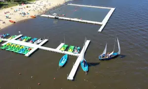 Na plaży i w wodzie widać ludzi, łódki, rowery wodne i pływający basen. To idealne miejsce na wypoczynek, jak kokotek łowisko Leśnica.