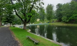 Spokojne stawy w Lądku-Zdroju, otoczone zielenią, zapraszają do odpoczynku. W oddali widać basen.