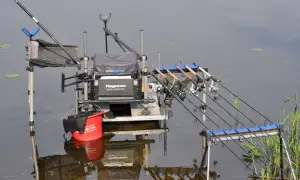 Gotowe stanowisko method feeder z kilkoma wędkami i czerwonym wiadrem, gotowe do łowienia ryb.