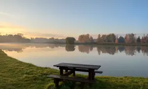 Poranek nad jeziorem, idealne miejsce na dzikie łowiska mazowieckie. Drewniana ławka i stół czekają na wędkarzy.
