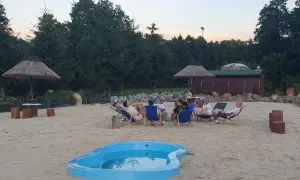 Relaks na piasku w Krężnicy Jarej. Grupa przyjaciół odpoczywa na leżakach przy małym basenie, w tle drewniana sauna i palmy.