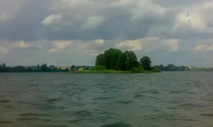 Spokojne jezioro Głuszyńskie, idealne na wędkowanie. Na horyzoncie zielone drzewa i chmury.