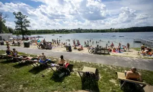 Tłum ludzi odpoczywa na plaży nad jeziorem Kierskim Małym. Słońce świeci, a chmury tworzą malowniczy krajobraz.
