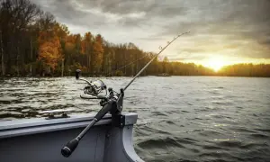 Wędka na łodzi, jesienne Mazury zachęcają, gdzie na ryby? Słońce zachodzi nad wodą, drzewa mienią się kolorami.