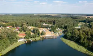 Widok z lotu ptaka na jezioro, plażę z ludźmi, kemping i las. Sprawdź jezioro przechlewskie cennik na wakacje.