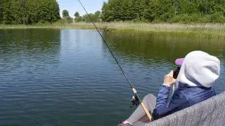 Osoba łowi ryby nad jeziorem, ciesząc się spokojem. Posiada zezwolenie PZW Wrocław.