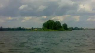 Spokojne jezioro Głuszyńskie, idealne na wędkowanie. Na horyzoncie zielone drzewa i chmury.