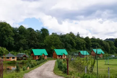 Gospodarstwo Jabłonica Ruska: malownicze drewniane domki z zielonymi dachami, staw, las i boisko.
