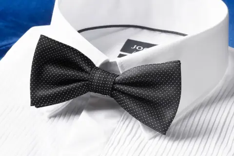 Czarna mucha w kropki na białej koszuli. Dowiedz się, jak założyć muchę, by wyglądać elegancko.