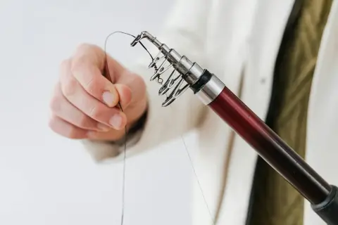 Dłoń trzymająca żyłkę przy końcu wędki z przelotkami.