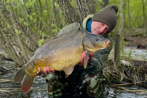 Wędkarz z dumą prezentuje okazałego karpia złowionego podczas nocnego łowienia. To prawdziwy skarb z fisch camp!