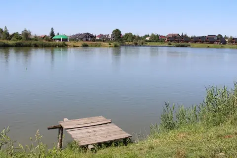 Drewniany pomost nad spokojnym jeziorem z domkami w tle.