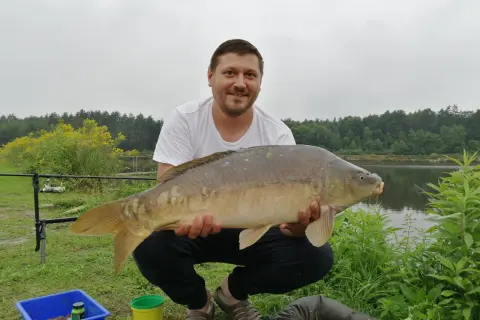 Szczęśliwy wędkarz z okazałym karpiem złowionym na łowiskach karpiowych podkarpackich.