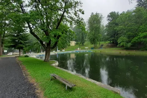 Spokojne stawy w Lądku-Zdroju, otoczone zielenią, zapraszają do odpoczynku. W oddali widać basen.