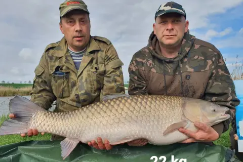 Dwóch wędkarzy prezentuje imponującego karpia o wadze 22 kg, złowionego na łowisku Nowe Żukowo.