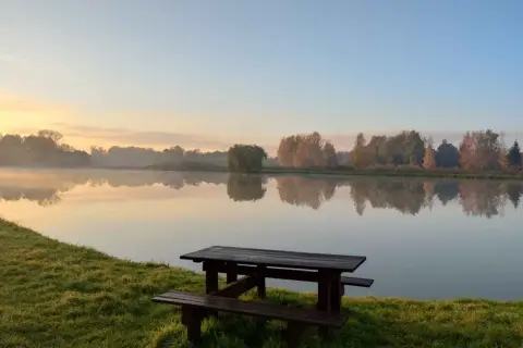Poranek nad jeziorem, idealne miejsce na dzikie łowiska mazowieckie. Drewniana ławka i stół czekają na wędkarzy.