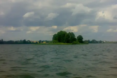 Spokojne jezioro Głuszyńskie, idealne na wędkowanie. Na horyzoncie zielone drzewa i chmury.
