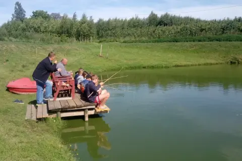 Dzieci i dorośli łowią ryby na drewnianym pomoście. Malownicze łowisko pod lasem Bielany Wrocławskie.
