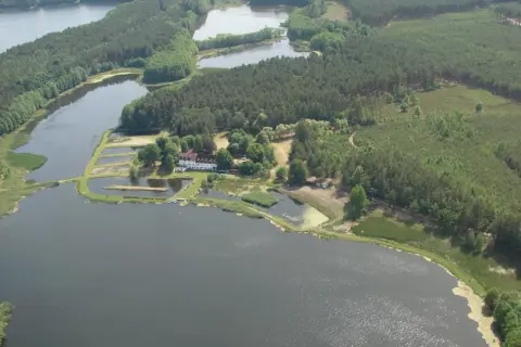 Agroturystyka Wilcze Doły: malowniczy krajobraz z jeziorami, lasami i zabudowaniami. Idealne miejsce na wypoczynek.