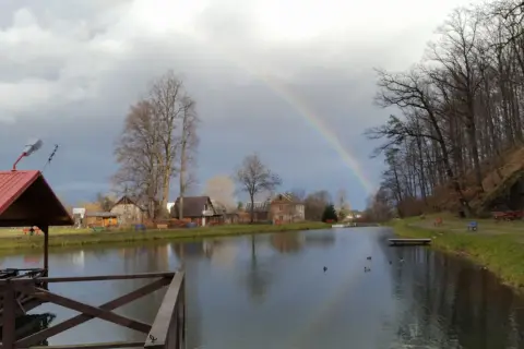 Tęcza nad jeziorem u Bodzia Moszczanka. W oddali domki, po prawej las i ławki.