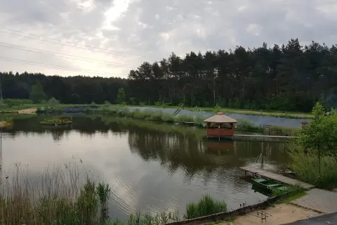 Malownicze łowisko Trzy Stawy z altaną na wodzie, małą wyspą i zieloną łódką przy pomoście.