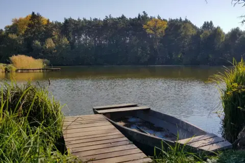 Łowisko agroturystyczne z łódką przy pomoście. Stawy otoczone lasem, jesienne barwy drzew.
