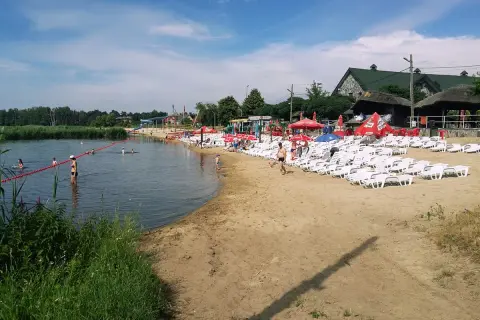 Słoneczny dzień na plaży, gdzie łowisko wilga wodna kraina zaprasza do kąpieli i relaksu. Leżaki i parasole czekają na plażowiczów.