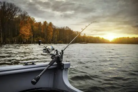 Wędka na łodzi, jesienne Mazury zachęcają, gdzie na ryby? Słońce zachodzi nad wodą, drzewa mienią się kolorami.
