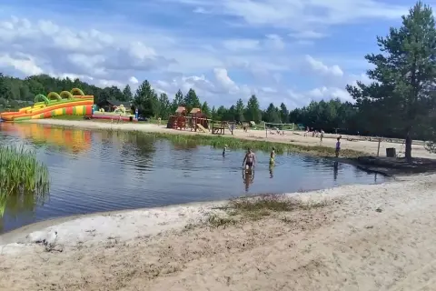 Sielska woda zaprasza do zabawy! Dzieci kąpią się, a w tle dmuchane zjeżdżalnie i plac zabaw. Sprawdź cennik i przyjedź!