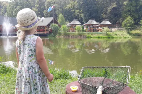 Dziewczynka w słomkowym kapeluszu patrzy na łowisko na wyspie Pokrzywna. Obok niej leży podbierak i kukurydza.
