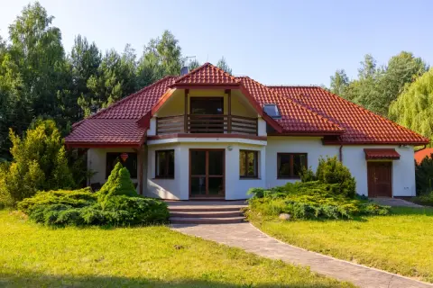 Urokliwa agroturystyka w dolinie stawów. Biały dom z czerwoną dachówką, otoczony zielenią, zaprasza na wypoczynek.