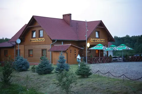 Drewniany budynek z napisem "Zajazd u Bartka" i zielonymi parasolami przed wejściem.