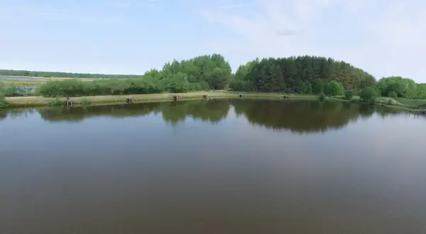 Widok na łowisko z pomostami i drzewami w tle, odbijającymi się w spokojnej wodzie.