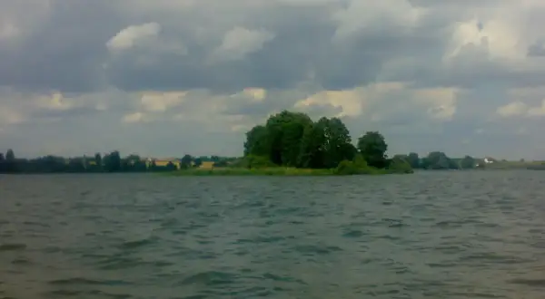 Spokojne jezioro Głuszyńskie, idealne na wędkowanie. Na horyzoncie zielone drzewa i chmury.