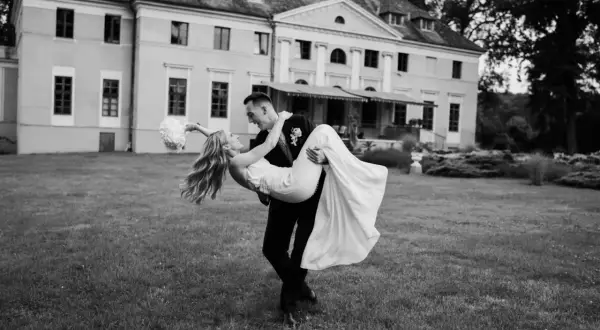 Pan młody niesie pannę młodą na rękach przed starym młynem nad Tywą.