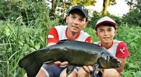 Dwóch wędkarzy z dumą prezentuje lina złowionego na zestaw spławikowy.