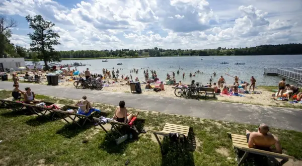 Tłum ludzi odpoczywa na plaży nad jeziorem Kierskim Małym. Słońce świeci, a chmury tworzą malowniczy krajobraz.