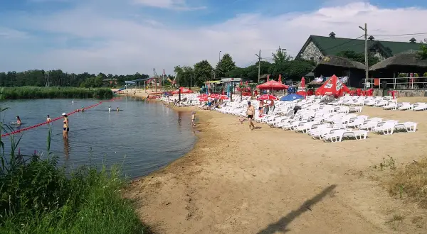 Słoneczny dzień na plaży, gdzie łowisko wilga wodna kraina zaprasza do kąpieli i relaksu. Leżaki i parasole czekają na plażowiczów.
