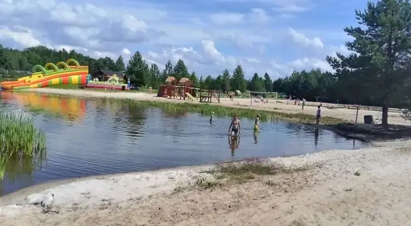 Sielska woda zaprasza do zabawy! Dzieci kąpią się, a w tle dmuchane zjeżdżalnie i plac zabaw. Sprawdź cennik i przyjedź!