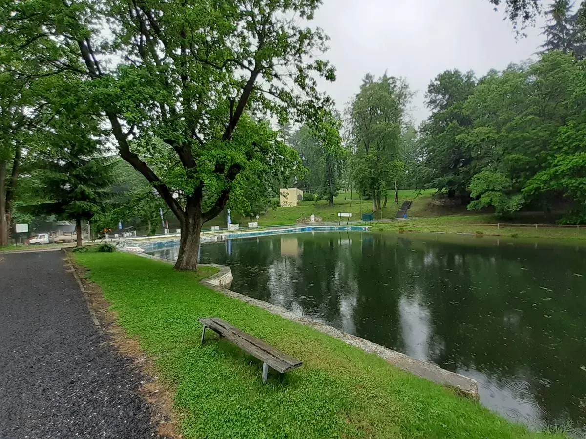 Spokojne stawy w Lądku-Zdroju, otoczone zielenią, zapraszają do odpoczynku. W oddali widać basen.
