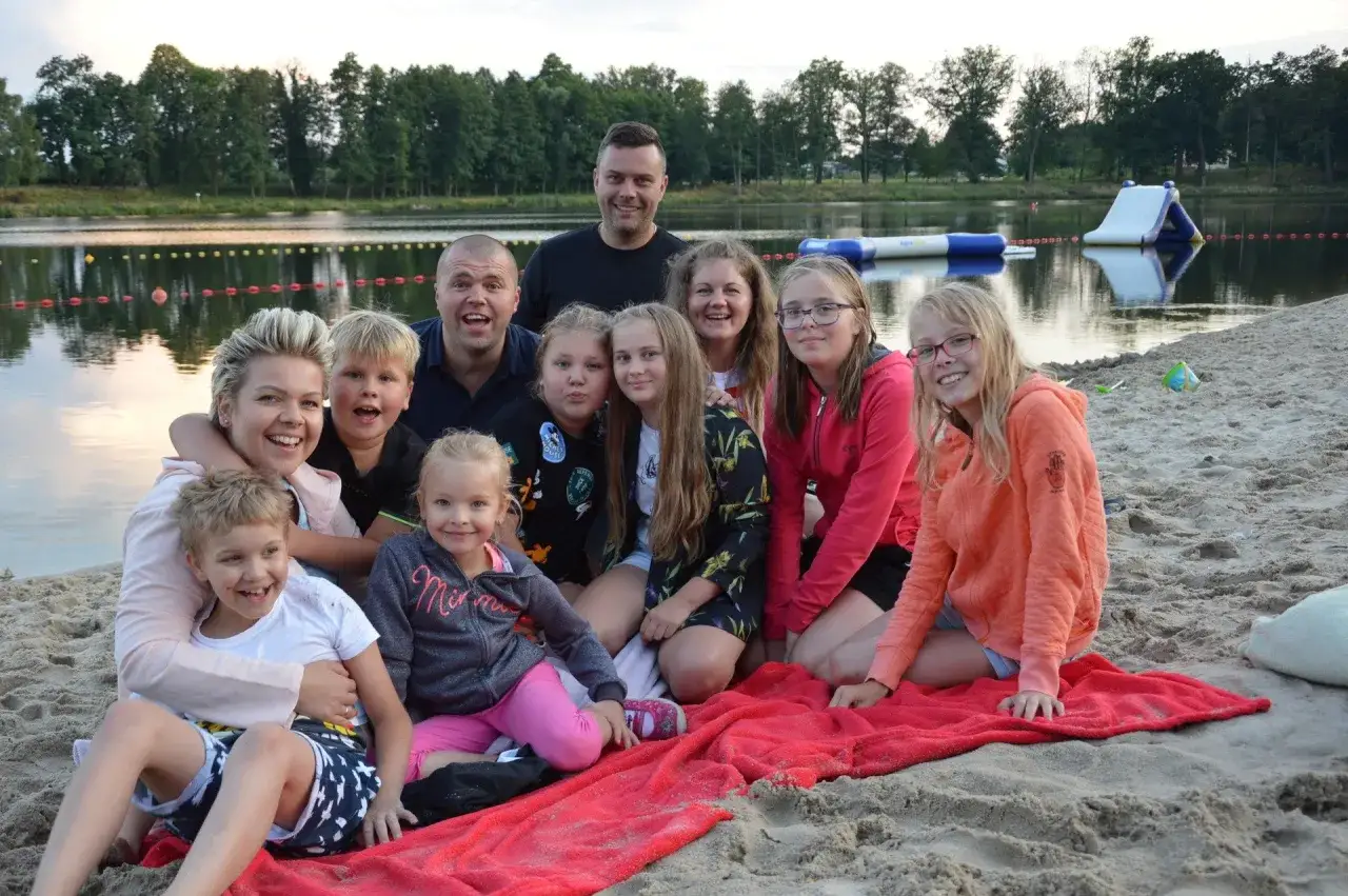 Rodzina i przyjaciele cieszą się wspólnym wypoczynkiem na plaży zalew Małomice. W tle widać wodę i dmuchane atrakcje.