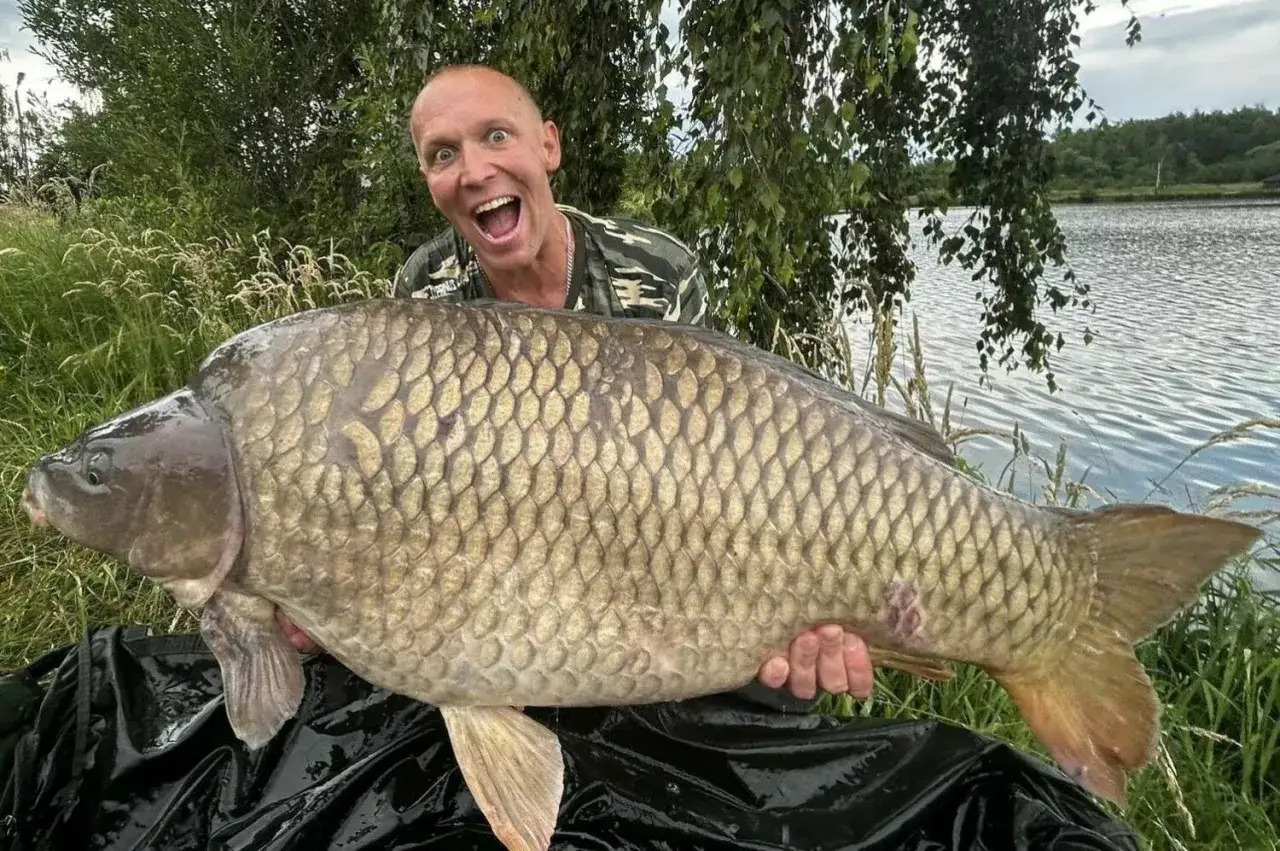 Szczęśliwy wędkarz z gigantycznym karpiem złowionym na łowisku Orle Stawy. Ryba jest ogromna, a mężczyzna ma szeroki uśmiech.