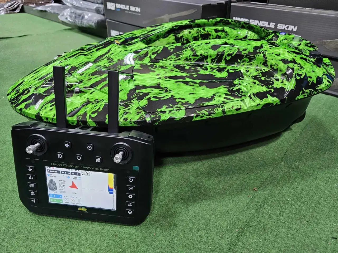 Łódka zanętowa z zielonym wzorem płomieni i pilotem z ekranem pokazującym GPS.