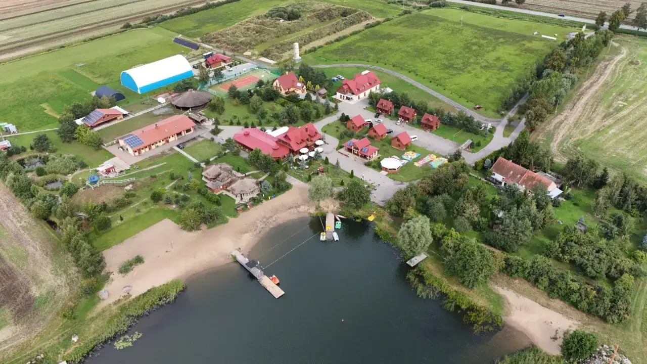 Malownicza jeziorna osada Gnojewo z piaszczystą plażą, pomostami i licznymi budynkami wypoczynkowymi.