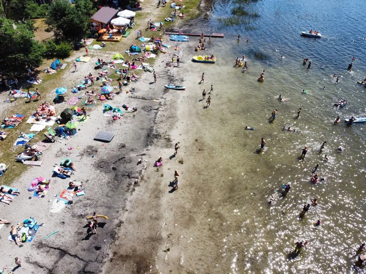 Ludzie odpoczywają na piaszczystej plaży nad jeziorem piaskowym Zamza. Kąpielisko tętni życiem, woda jest pełna kąpiących się.