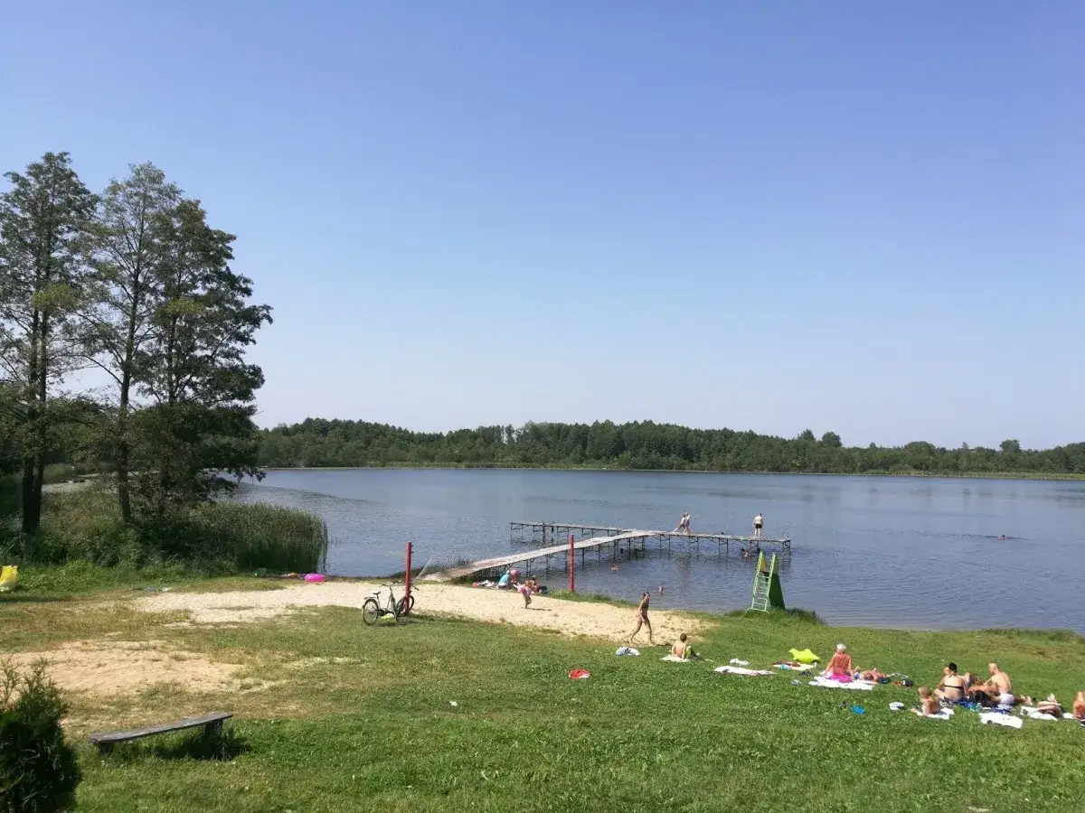 Słoneczny dzień nad jeziorem głębokim lubelskim. Ludzie odpoczywają na plaży i w wodzie, korzystając z pomostu i pięknej pogody.