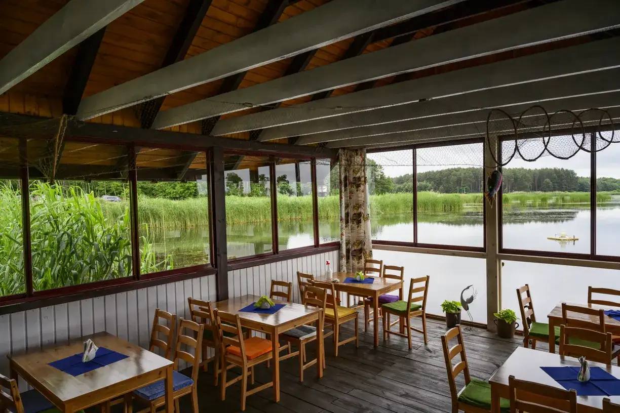 Wnętrze restauracji z widokiem na jezioro. Stoły i krzesła czekają na gości w gospodarstwie rybackim Stobno.