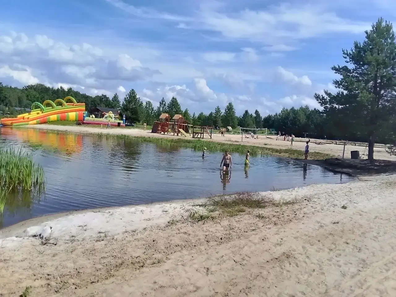 Sielska woda zaprasza do zabawy! Dzieci kąpią się, a w tle dmuchany zamek i plac zabaw. Sprawdź cennik i przyjedź!